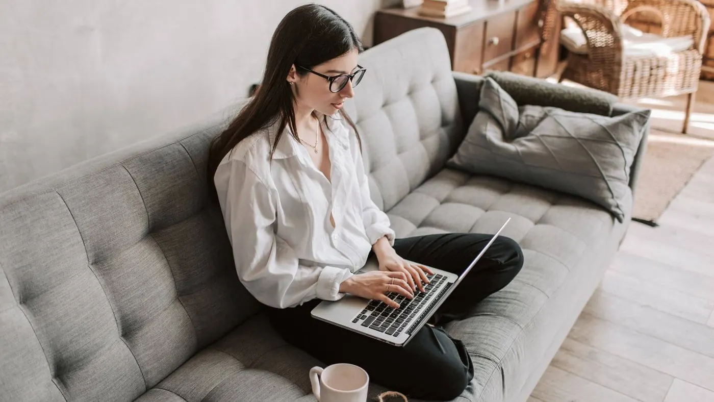 Woman working while sitting on her couch.